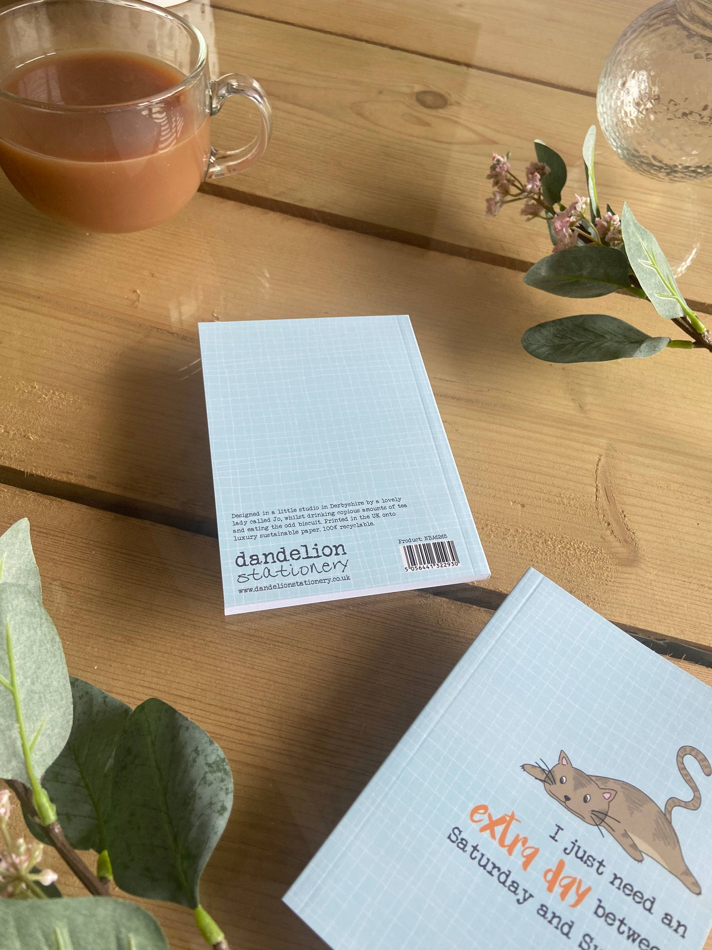 Notebook with a cat illustration on a wooden table with a cup of tea and flowers.