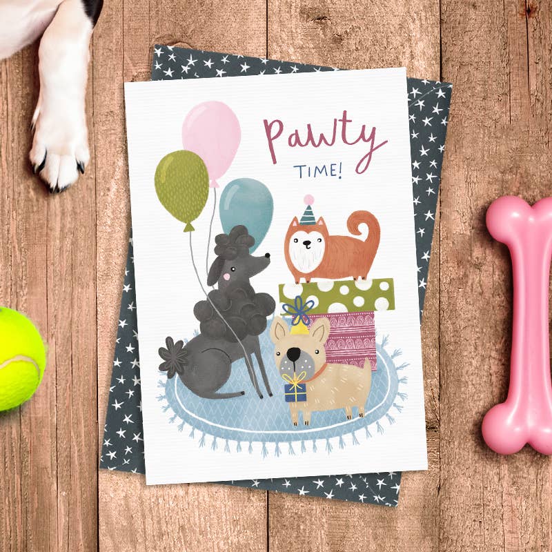 Card with cartoon animals and 'Pawty Time!' text on a wooden surface with dog toys.