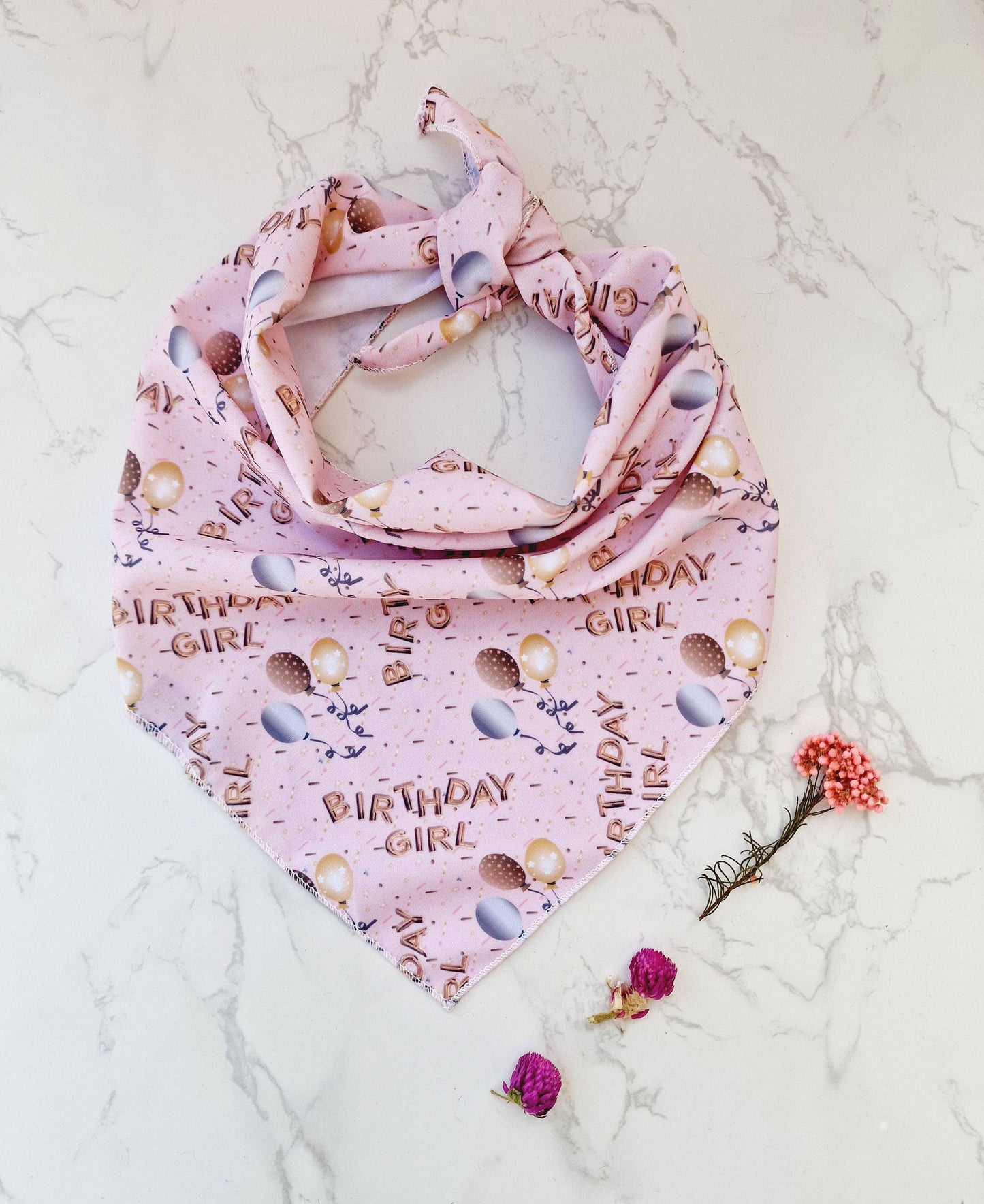 Pink dog bandana with 'Birthday Girl' text on a marble surface