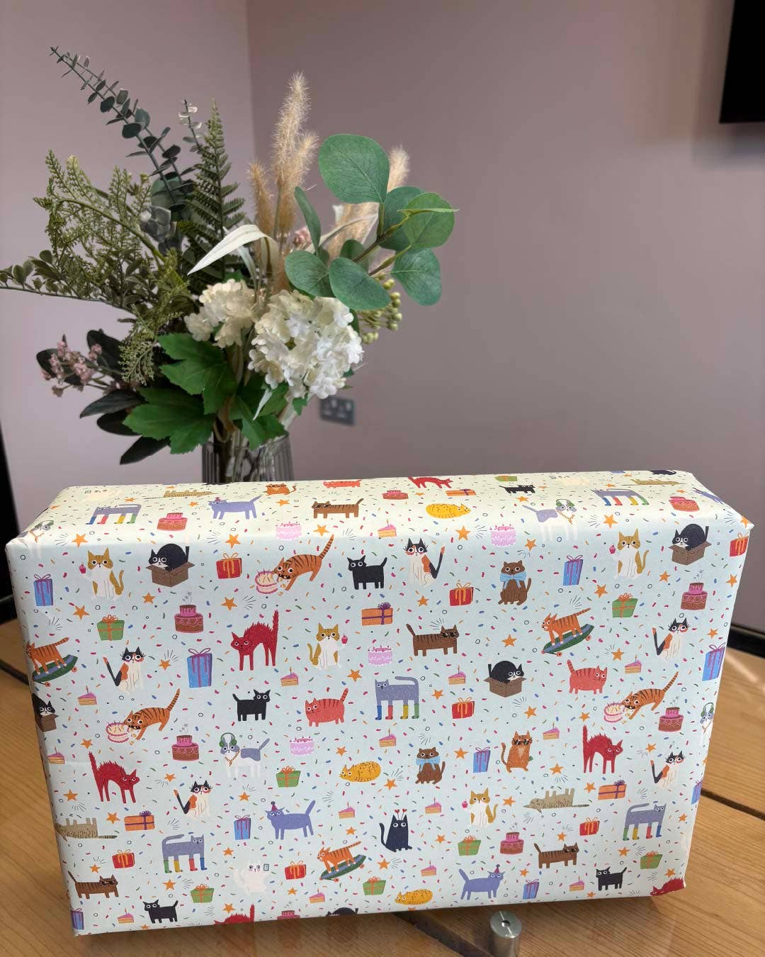 Box with a colourful cat pattern on a wooden surface with flowers in the background