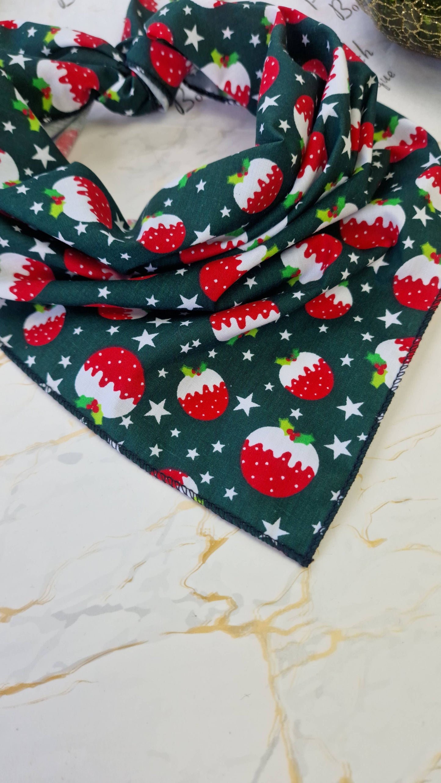 Christmas-themed dog bandana with red berries and green leaves on a marble surface.