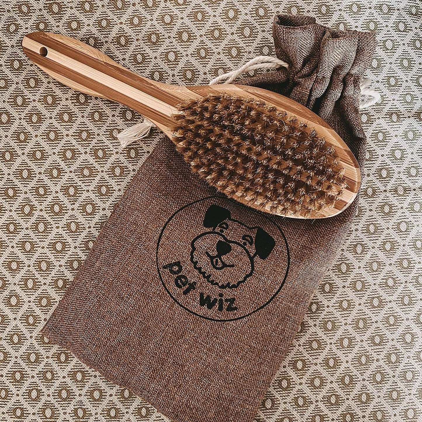 Wooden pet brush on a brown towel with 'Pet Wiz' logo against a patterned background