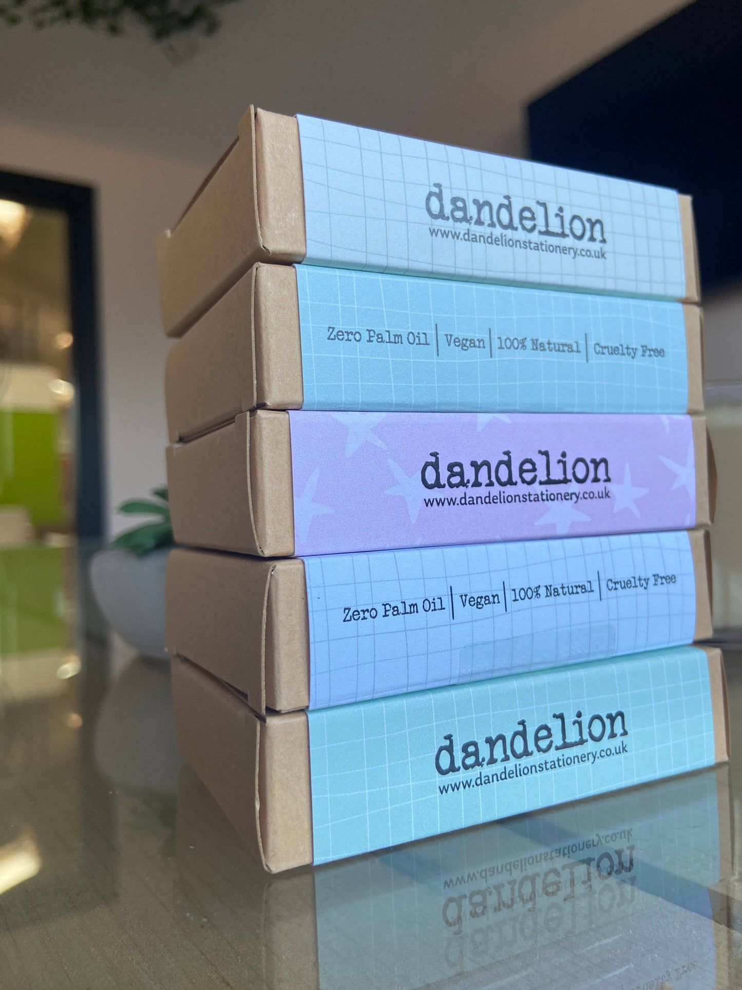 Stack of dandelion product boxes on a reflective surface with a blurred indoor background