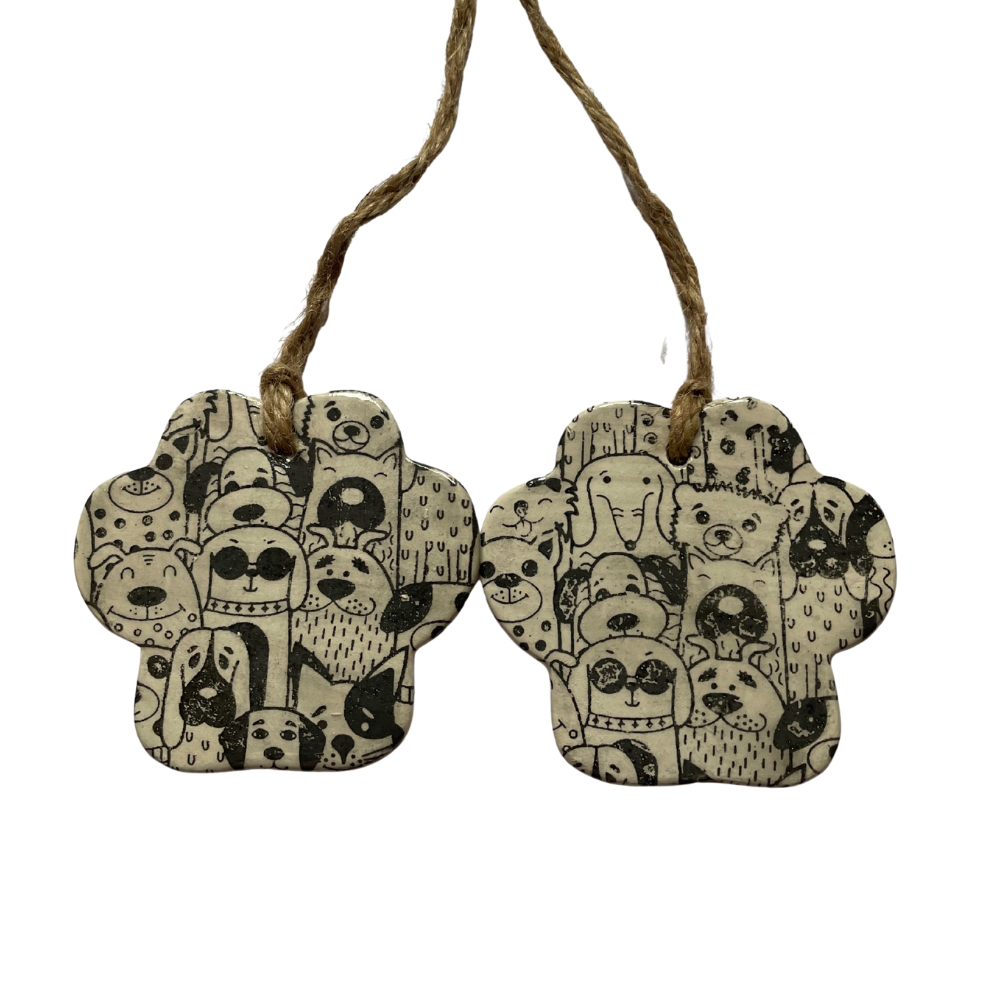 Two ceramic paw-shaped ornaments with black and white dog patterns hanging from a string on a white background.