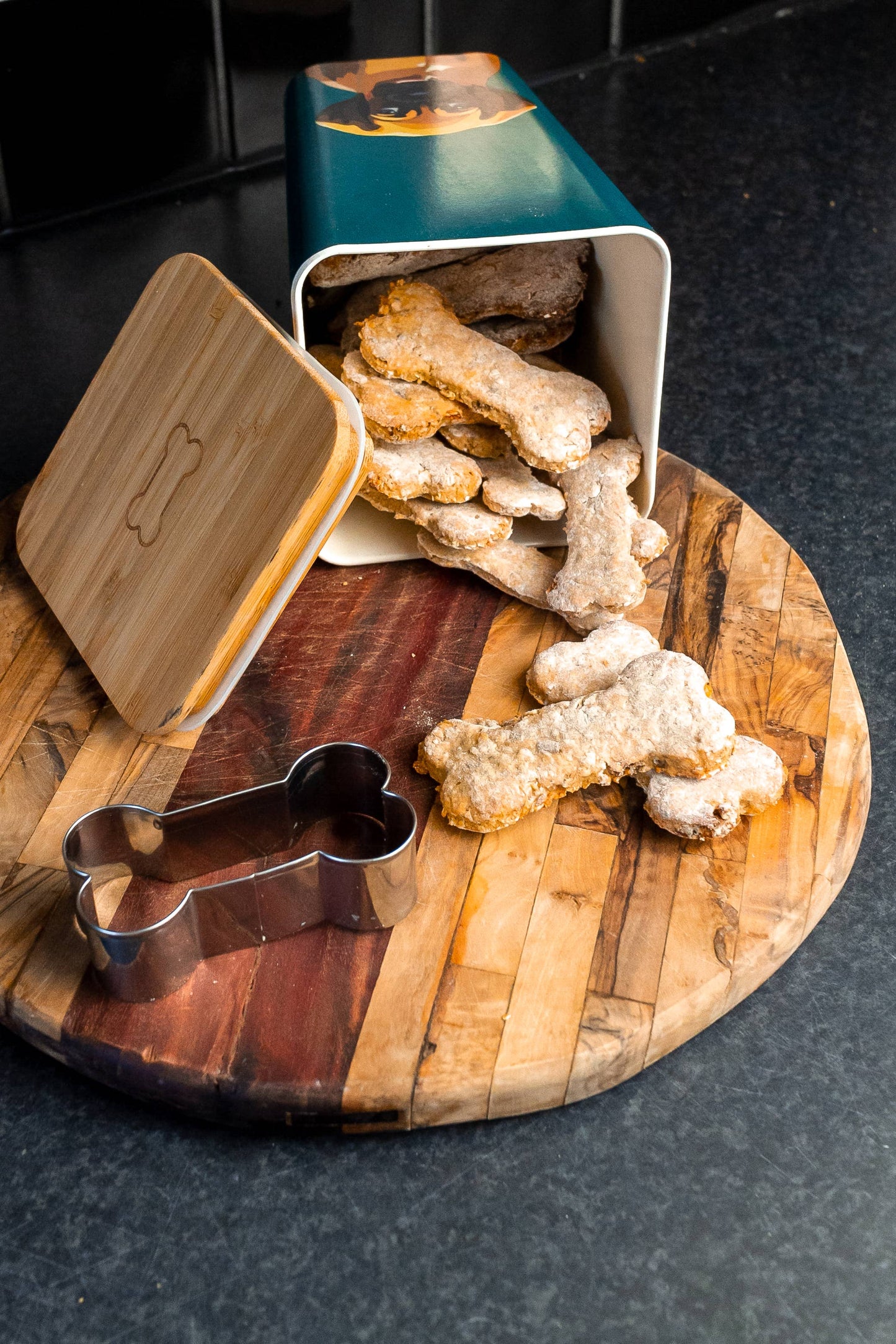 Dog treats on a wooden board with a cookie cutter and bamboo tin.