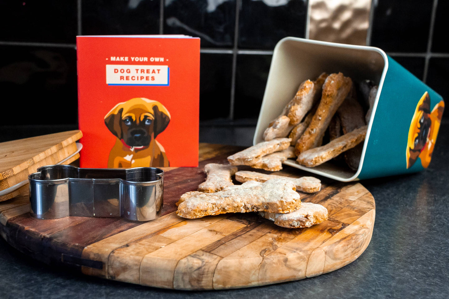 Dog treat-making setup with cookie cutter, wooden board, and recipe book.