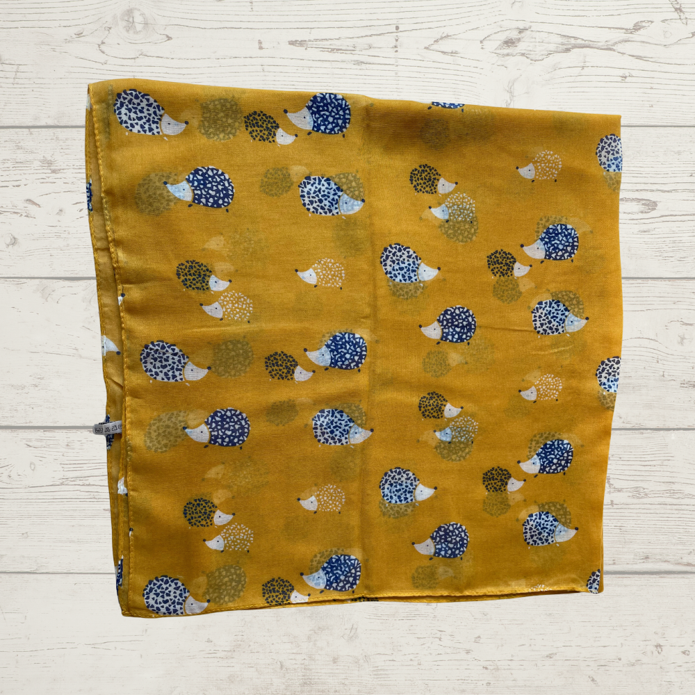 A mustard yellow scarf with images of hedgehogs printed all over it laid on a wooden surface.