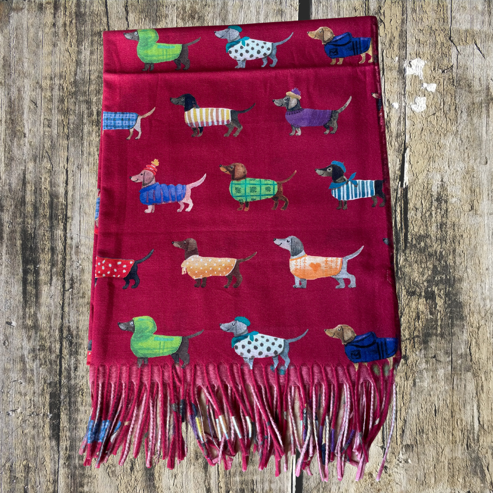 a red scarf with images of sausage dogs in coats printed on it laid a wooden surface