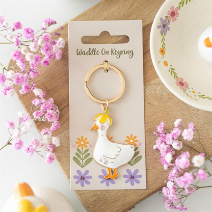 Keyring with duck design on a decorative card, surrounded by flowers on a wooden surface.