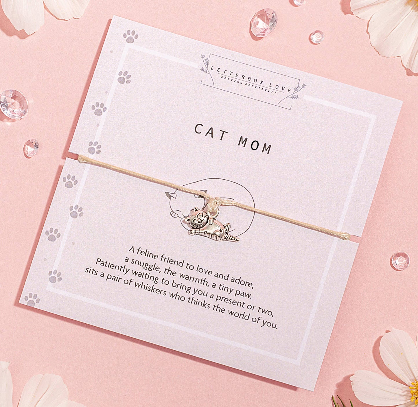A silver-colored cat pendant on a nude-colored string bracelet, presented on a card with 'CAT MOM' text and a descriptive poem.