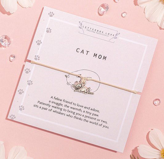 A silver-colored cat pendant on a nude-colored string bracelet, presented on a card with 'CAT MOM' text and a descriptive poem.