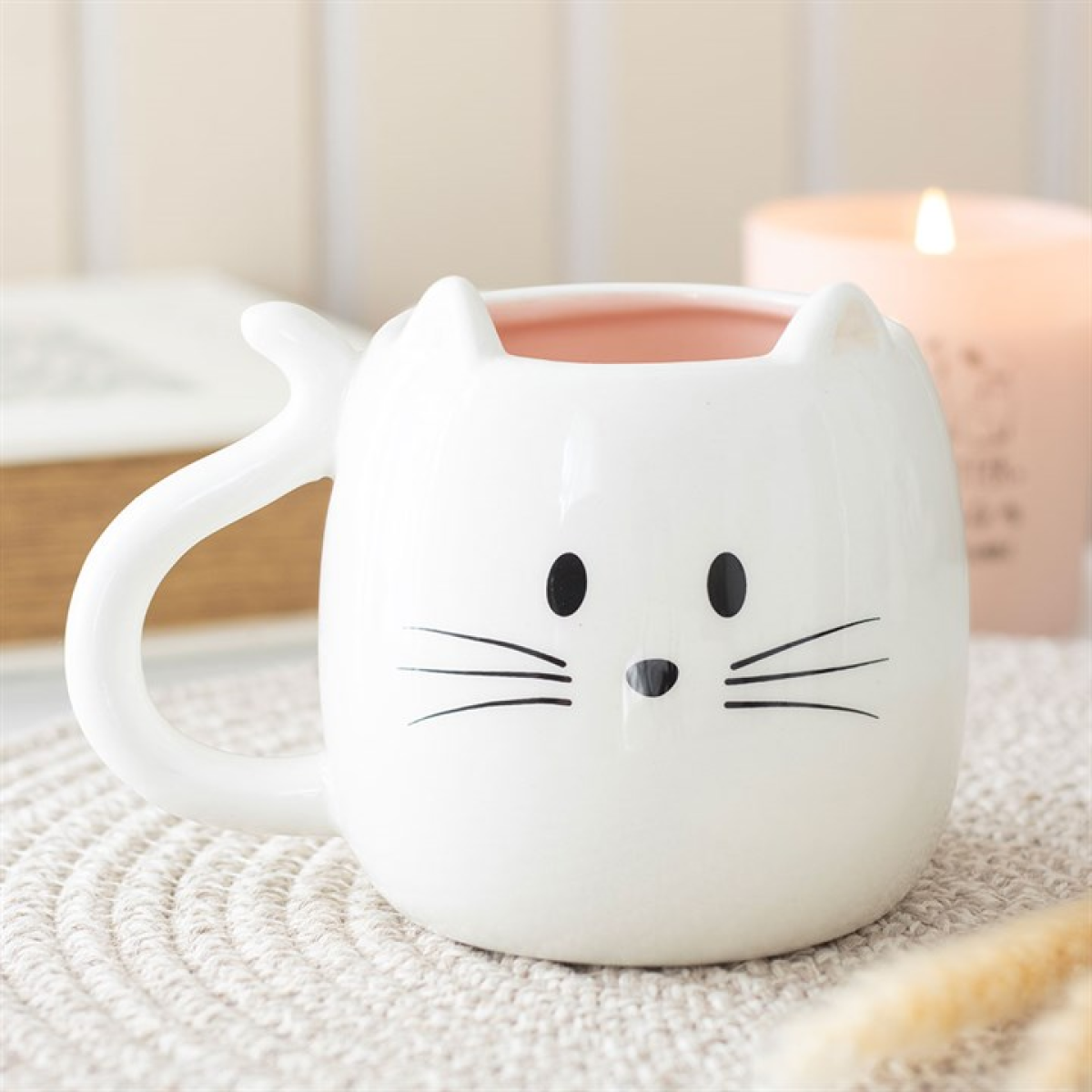 White cat-shaped mug on a textured surface with a blurred candle in the background