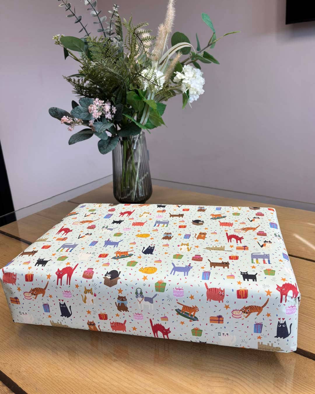 Box with cat pattern on a wooden surface with flowers in the background