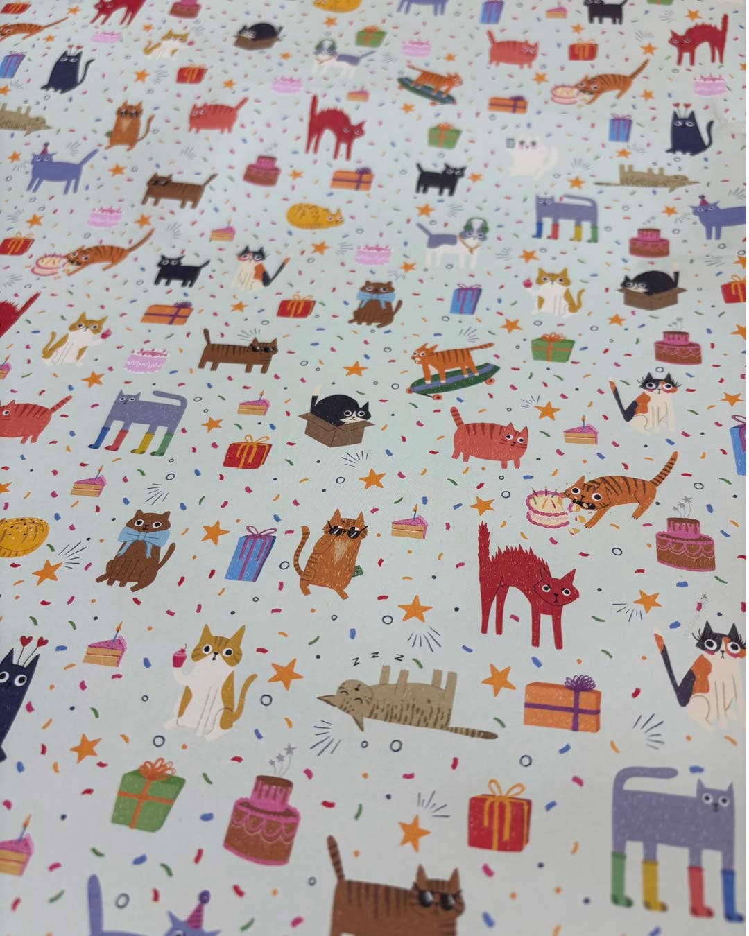 Patterned gift wrap with colourful cats and various objects on a light background