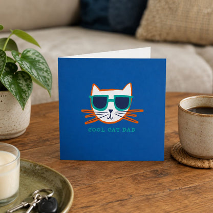 Greeting card with cool cat dad design on a wooden table with a cup and plant.