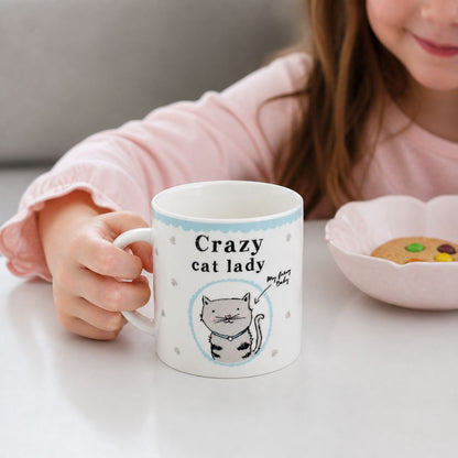 Person holding a mug with 'Crazy cat lady' text and a cat illustration, sitting at a table with cookies.