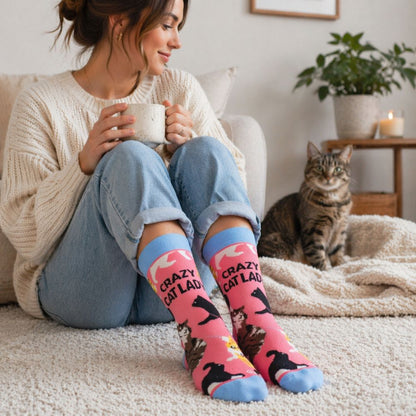 Woman wearing pink 'Crazy Cat Lady' socks sitting on a couch with a cat and holding a mug.