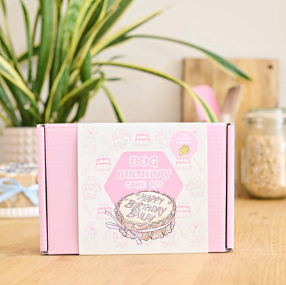 Dog birthday cake kit box on a wooden surface with a plant in the background