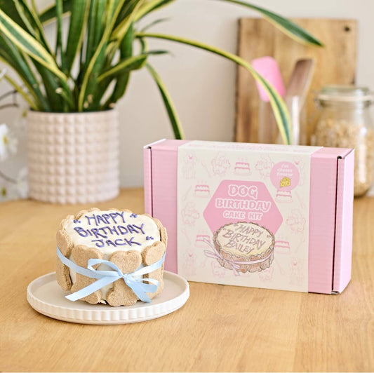 Dog birthday cake with 'Happy Birthday Jack' text next to a pink and white box on a wooden surface.