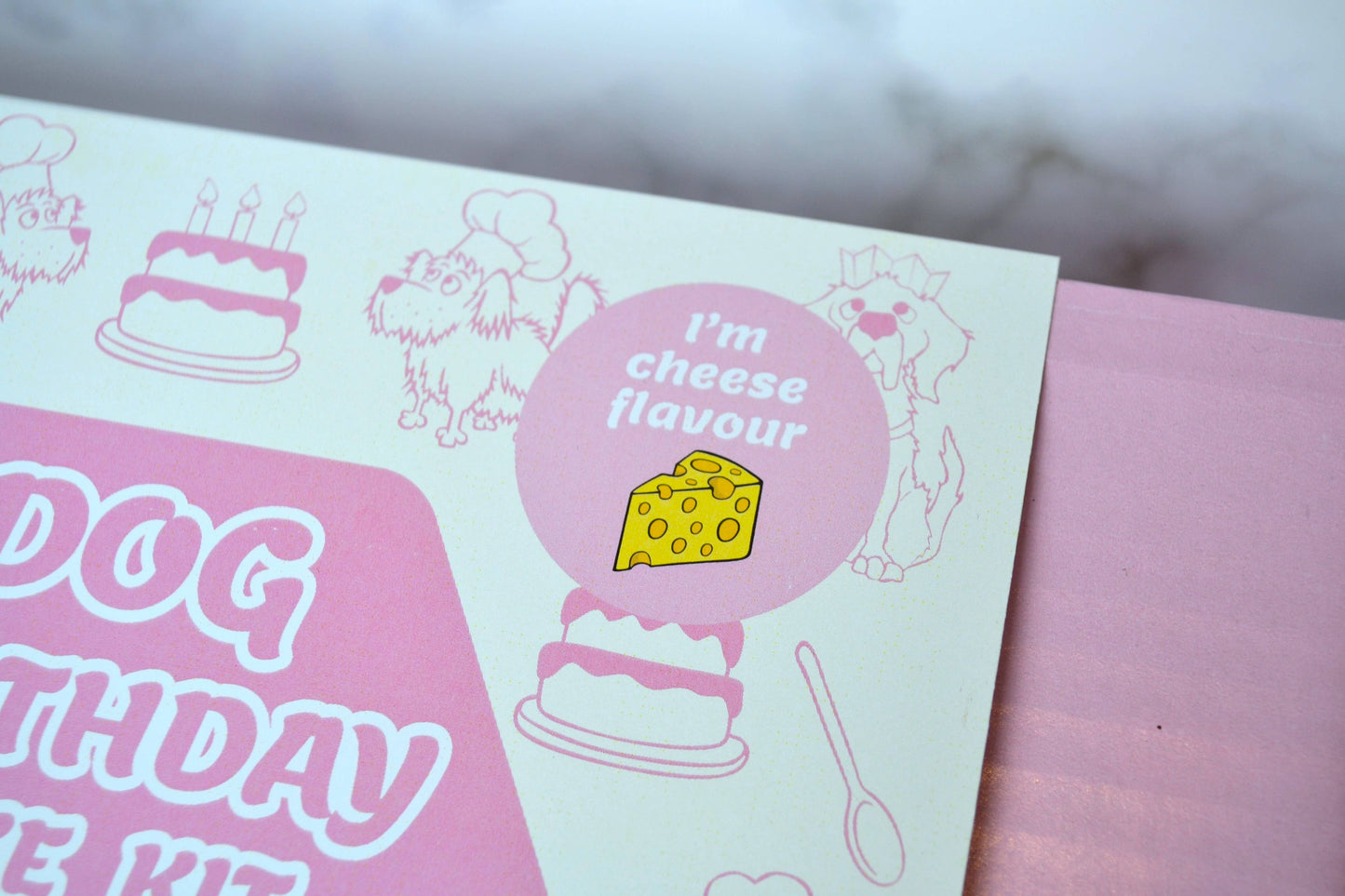 Pink and white dog birthday cake kit with cheese flavour label and cake illustrations.