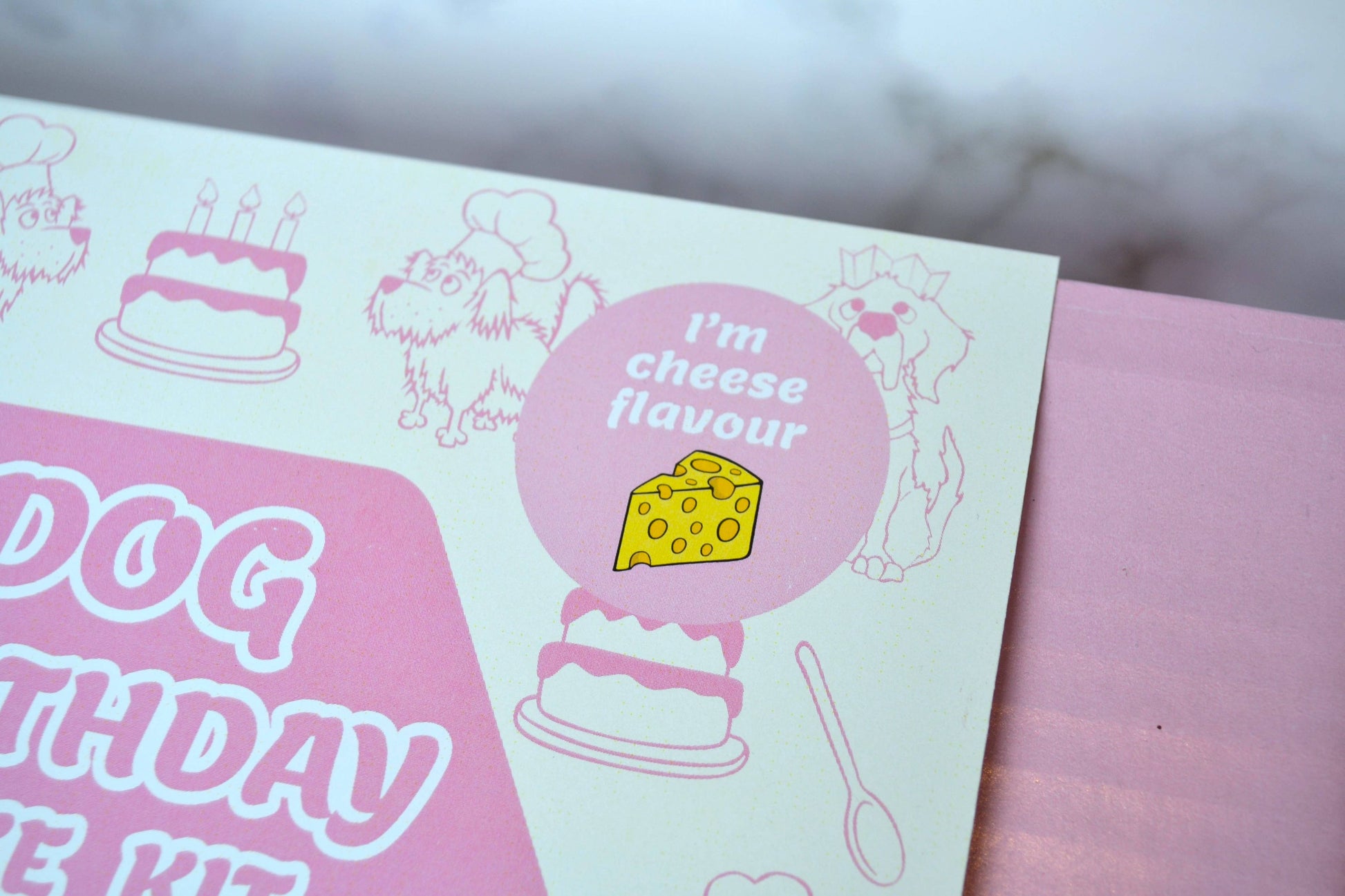 Pink and white dog birthday cake kit with cheese flavour label and cake illustrations.