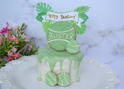 Green birthday cake with 'Happy Birthday Buster' topper on a marble surface with flowers.