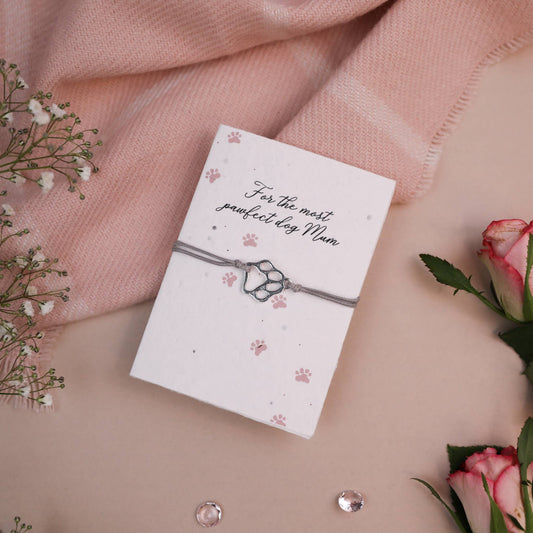 A set of a seeded card and a wish bracelet with a paw print charm on a card, presented on a pink background with some decorative flowers.