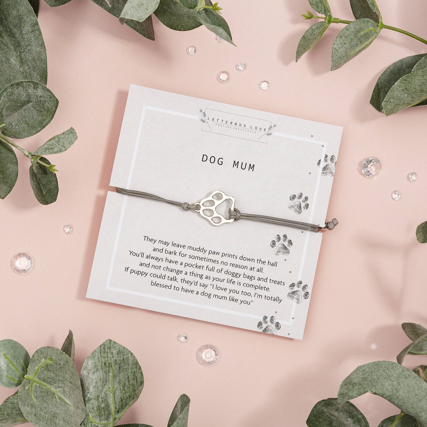 Adjustable bracelet with a dog paw print charm and a poem card, presented on a pink background with green leaves.