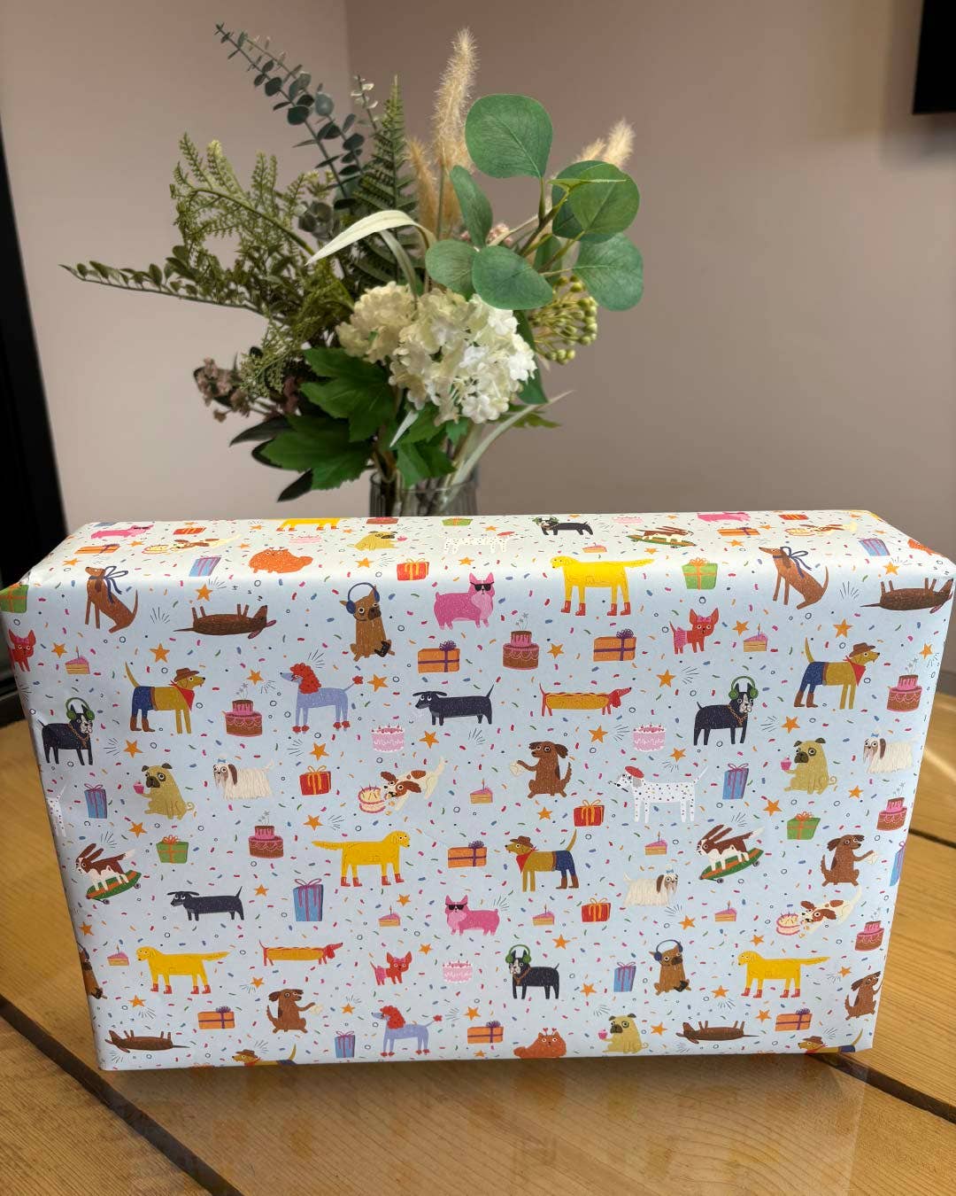 Box with dog patterned paper and a vase of flowers on a wooden surface