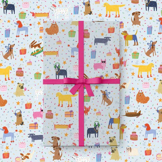 Gift wrapped in colorful dog-themed paper with a pink ribbon on a matching patterned background.
