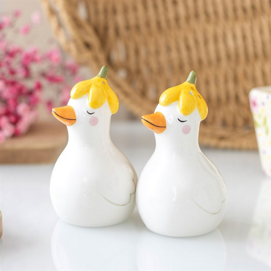 Two ceramic duck figurines with yellow hair and orange beaks on a white surface.