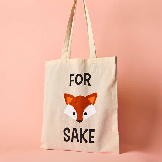 A beige cotton tote bag with the text 'FOR FOX SAKE' printed on the front, featuring a cartoon illustration of a fox's face.