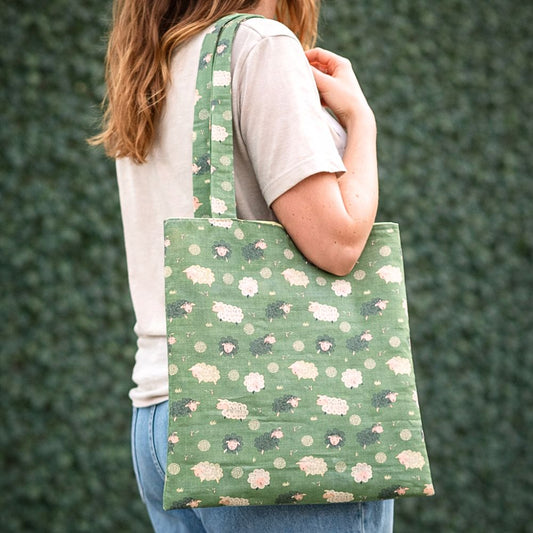 Person holding a green tote bag with sheep pattern against a green background