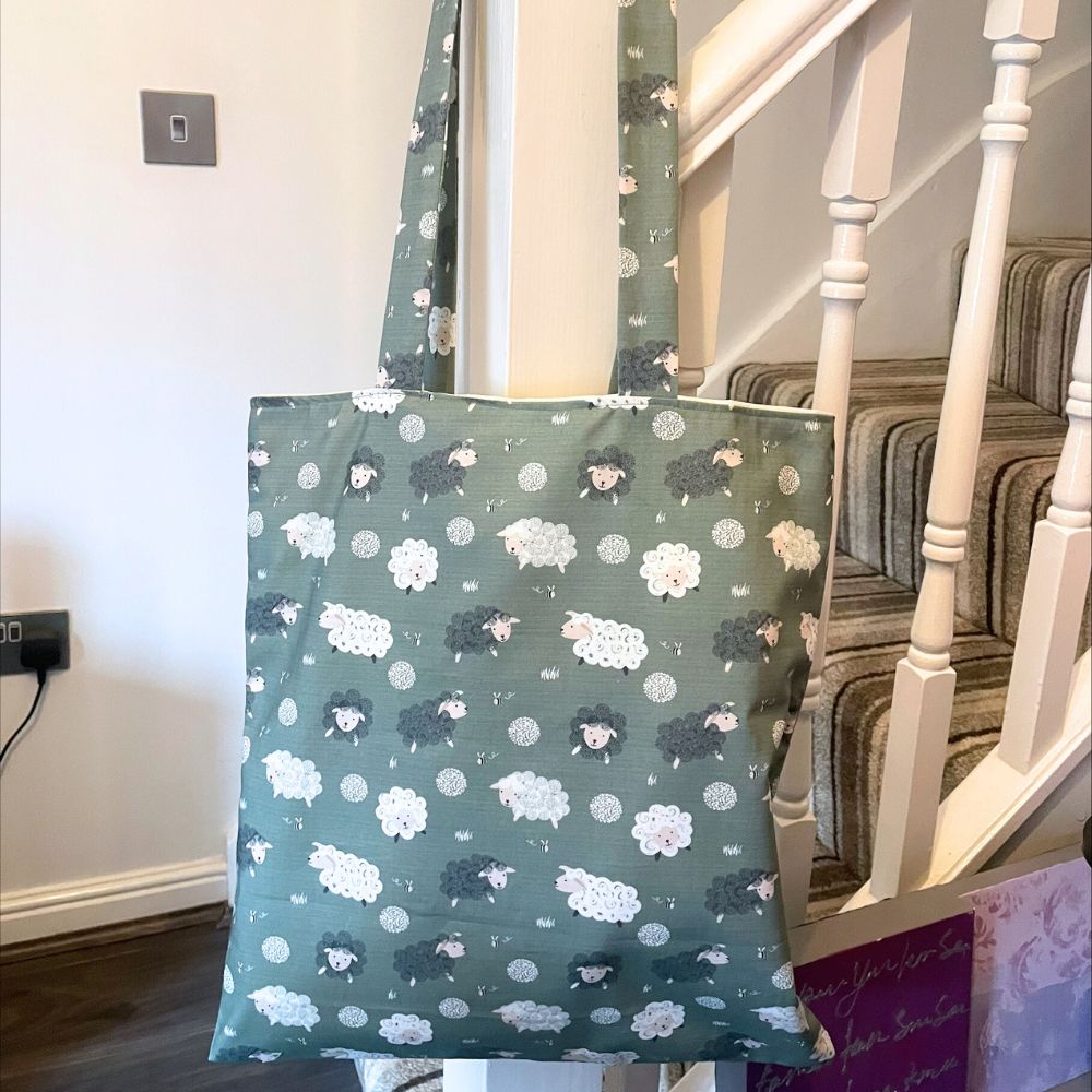 Green tote bag with sheep and flower pattern hanging on a staircase handrail.