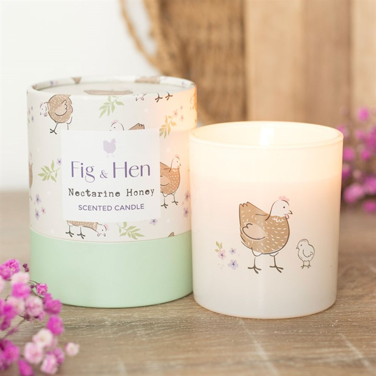Fig & Hen scented candle with packaging on a wooden surface with flowers.