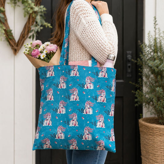 Person holding a blue tote bag with horse pattern, filled with flowers, against a door and plant background.