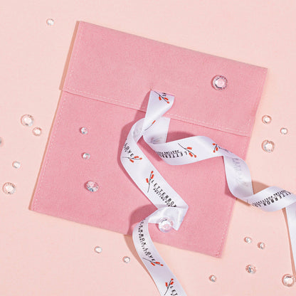 A pink velvet pouch with a white ribbon on a pink background, surrounded by water droplets creating a reflective effect.