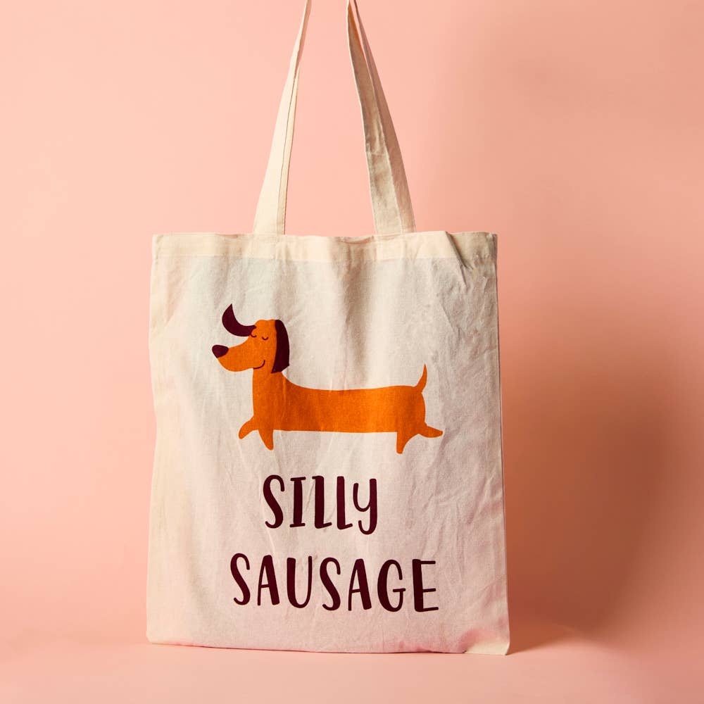 A white cotton tote bag with an illustration of a cartoon dog and the phrase 'SILLY SAUSAGE' printed on the front.