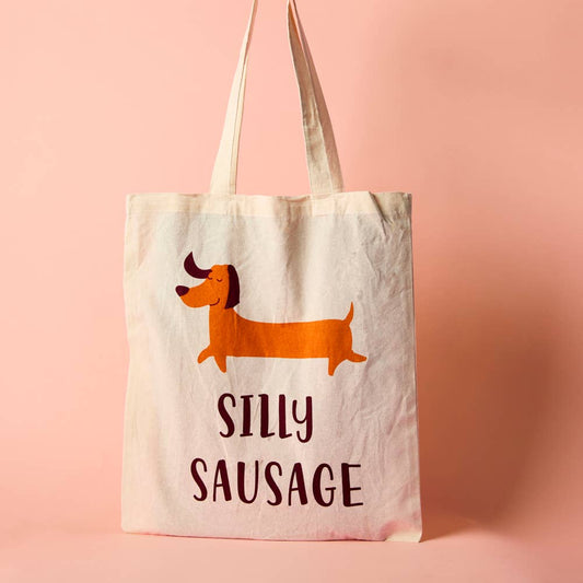 A white cotton tote bag with an illustration of a cartoon dog and the phrase 'SILLY SAUSAGE' printed on the front.