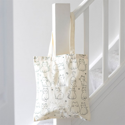 Tote bag with cat pattern hanging on a white railing.